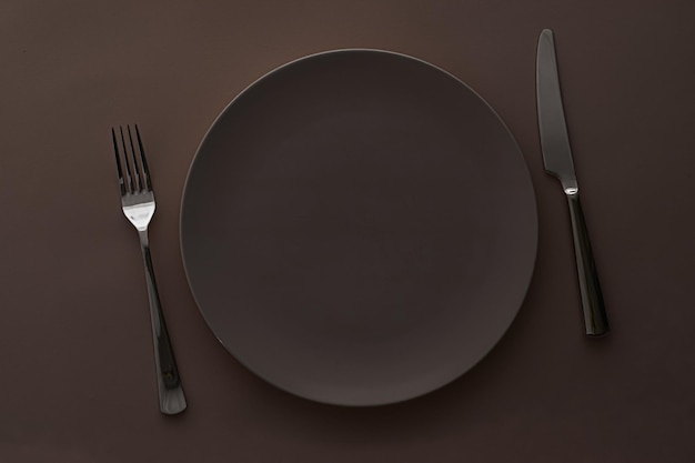 Empty plate and cutlery as mockup set on dark brown background top tableware for chef table decor and menu branding