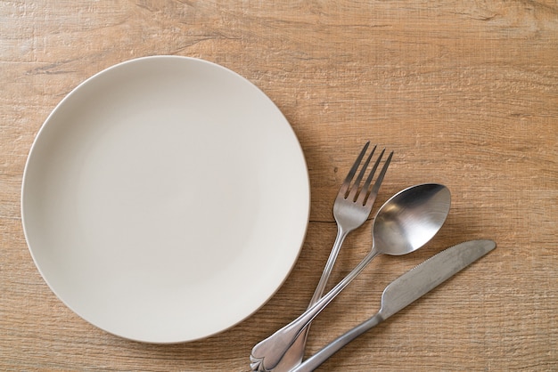 empty plate or dish with knife, fork and spoon on wooden table