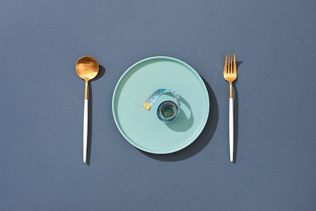 Empty plate with measuring tape, knife and fork. Diet food on a color table