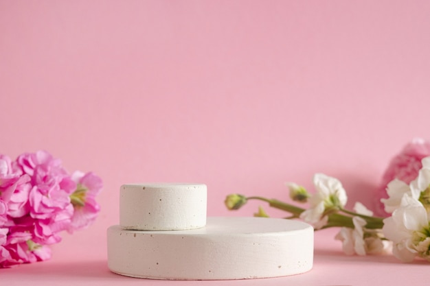 Empty podium for presentation of cosmetic products. Pastel flowers on pink background side view