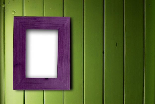 Empty purple frame fixed on a green wooden wall, the color of the inner part of the frame is white