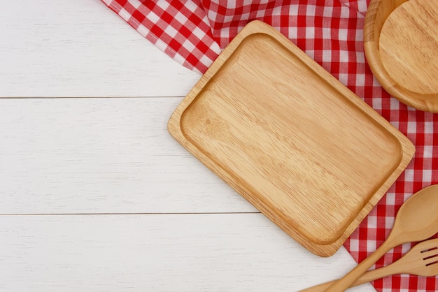 Empty rectangle wooden plate with spoon fork and red gingham tablecloth on white wooden table