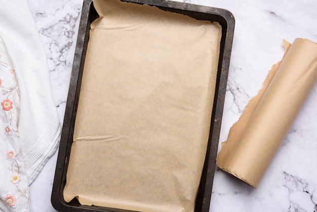 Empty rectangular metal baking sheet and roll of brown parchment paper , top view