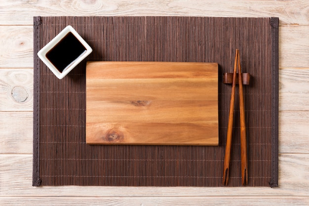 Empty rectangular wooden plate for sushi with sauce and chopsticks on wooden table, top view