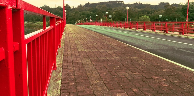 Empty red bridge with streetlights across lake with forest in background