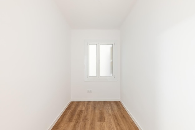 Empty room with laminate flooring newly painted white walls and bright window with frosted glass