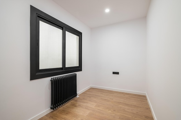 An empty room with a modern version of a plastic window with a black frame and opaque glass radiator