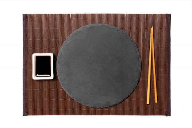 Empty round black plate with chopsticks and soy sauce, ginger on dark bamboo mat