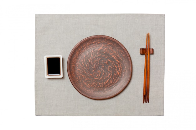 Empty round brown plate with chopsticks for sushi and soy sauce on grey napkin background. Top view with copyspace