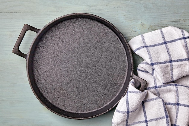 Empty round cast iron pan tea towel on a light blue wooden table