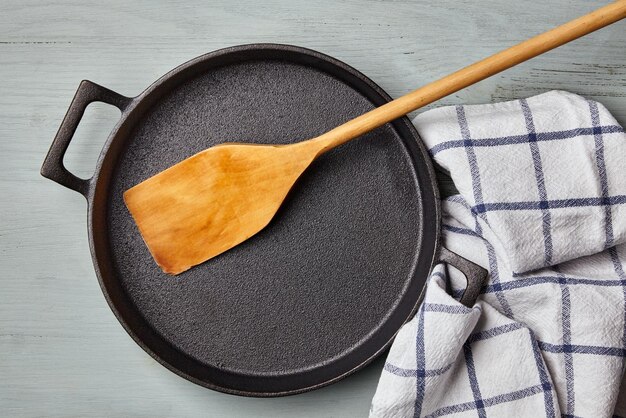 Empty round cast iron pan wooden spatula and tea towel napkin on a blue wooden table Template for laying out a dish