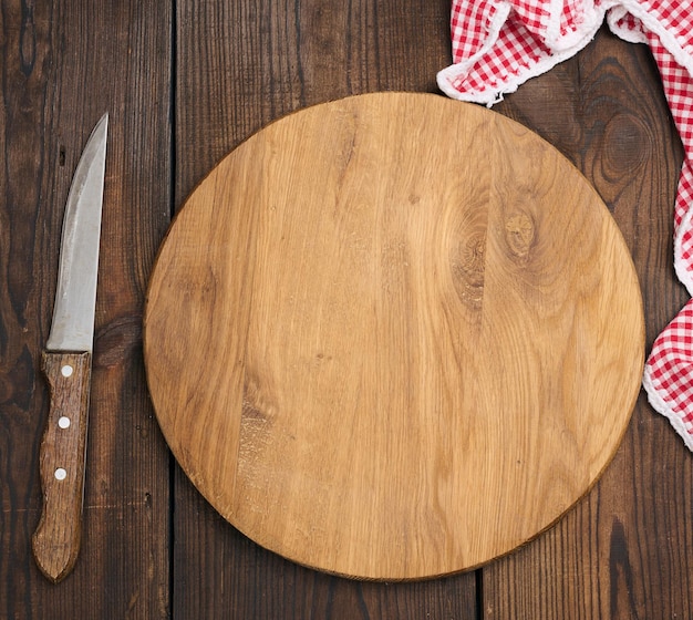 Empty round wooden cutting board and knife on brown table top view