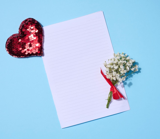 Empty sheet of paper gypsophila bouquet and red sequin heart on a blue background top view