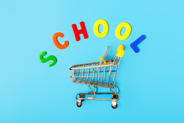 Empty shopping cart trolley and the word school of multicolored letters on a blue background Concept for a store of goods for school and education Sale and discount concept