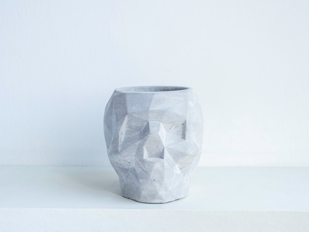 Empty skull shape concrete plant pot on white wooden shelf isolated on white wall. Small modern DIY cement planter trendy decoration.