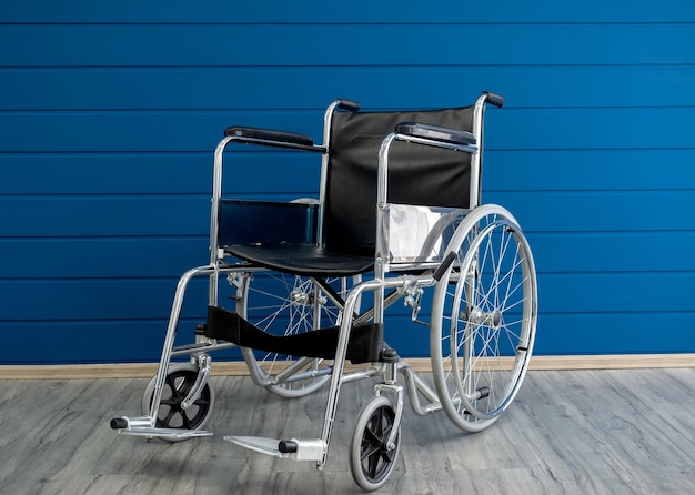 Empty steel wheelchair with black leather seat and backrest on the blue wooden plank wall background A chair with wheels for use as a transport by a person who unable to walk illness injury