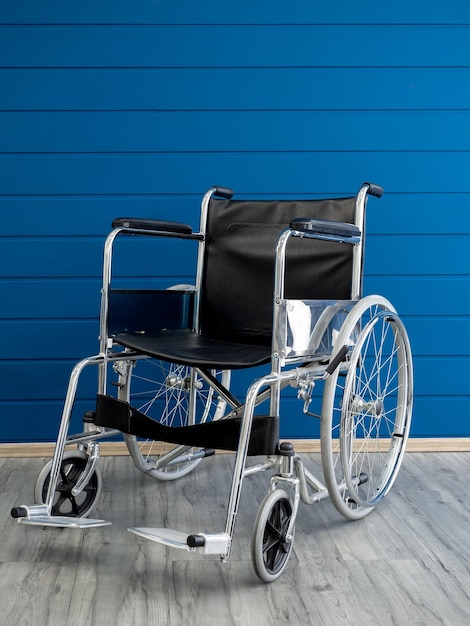 Empty steel wheelchair with black leather seat and backrest on the blue wooden plank wall background vertical style Chair with wheels for use as transport by person who unable walk illness injury