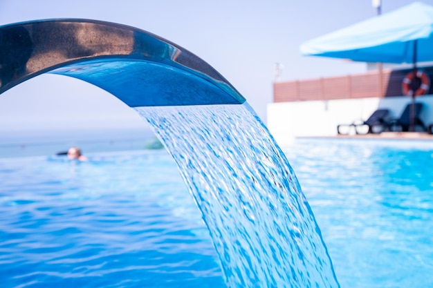 Empty Swimming pool with waterfall jet jacuzzi in actionSpa and wellness centerSeaside vacationhotel resort concept Reflection in blue clean sea water poolRelaxation pool in spa with waterfall