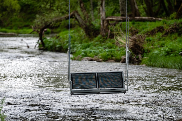 Empty swing hanging on ropes above a fast flowing river concept of active recreation