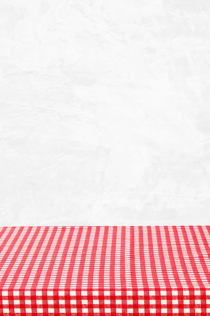 Empty table with red and white check pattern tablecloth over white wall background