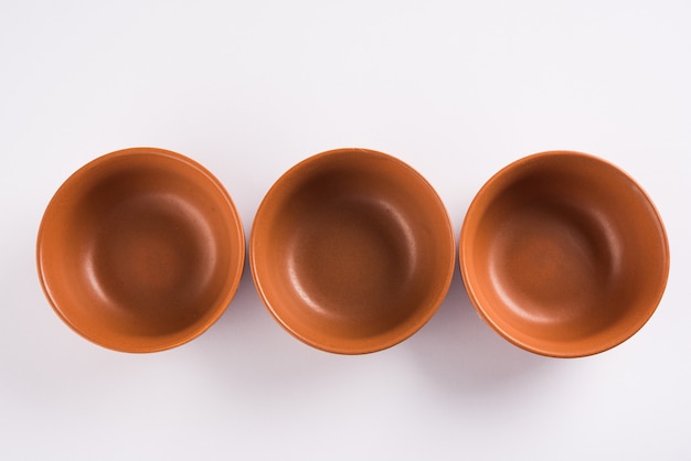 Empty terracotta dinnerware or dining set like plate, soup bowl, serving bowl, glass made up of brown clay, isolated over white