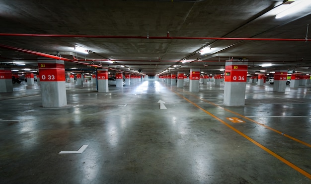 Empty underground car parking lot. Underground car parking garage at shopping mall or international airport. Indoor parking area. Concrete basement floor parking garage.