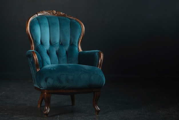 An empty vintage royal blue armchair against black background