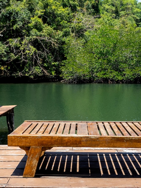 Empty vintage wooden bench on the wood terrace near the green river and mangrove jungle background on hot sunny day vertical style Empty space on the seat for place the product summer concept