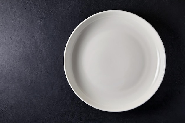 Empty white ceramic plate on a black stone table Top view with copy space