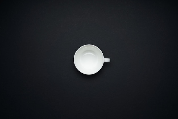 Empty white cup isolated on black background . Flat lay and top view with copy space .