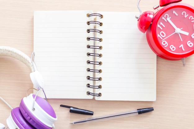 Empty white notebook with pen, alarm clock and headphone.