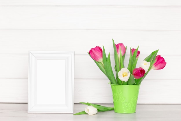 Empty white photo frame with tulip flower bouquet on table Light rustic interior