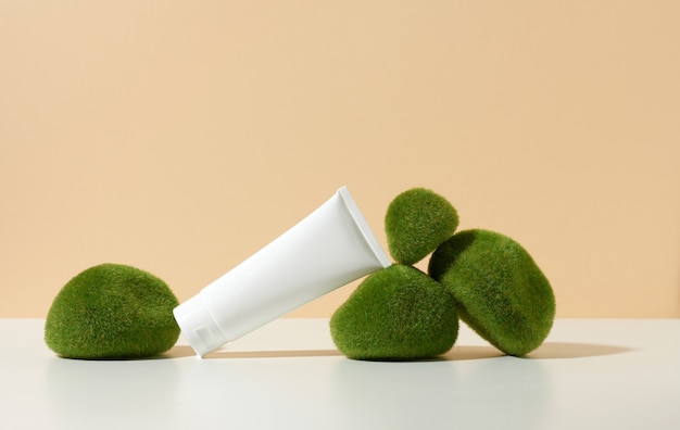 Empty white plastic tube near stones with moss on a beige background. Cosmetic products for branding gel, cream, lotion, shampoo. Mock up