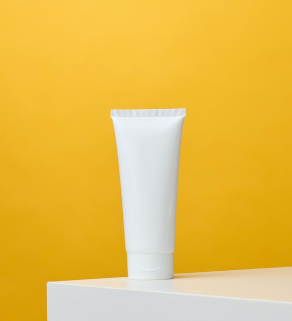 Empty white plastic tubes for cosmetics on a yellow background Packaging for cream gel serum advertising and product promotion