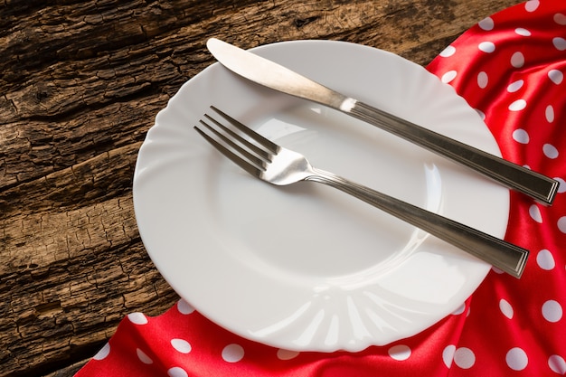 Empty white plate and cutlery on red napkin