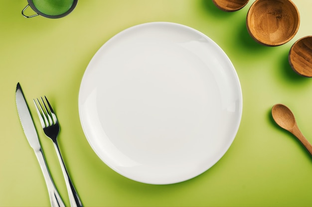 Empty white plate on the green table Top view Kitchen utensils beside like fork knife bamboo containers