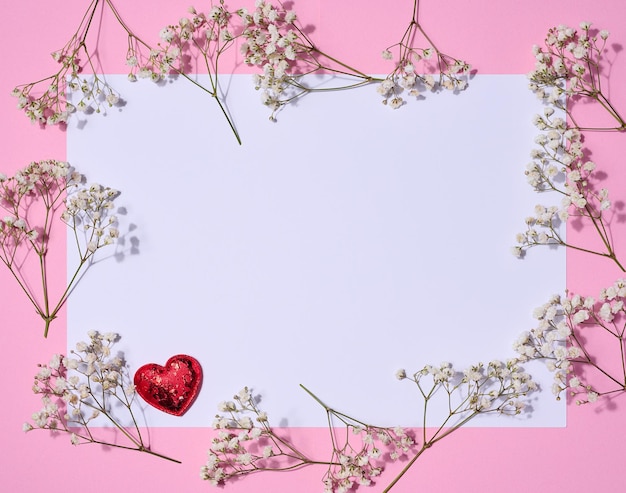 Empty white sheet of paper and gypsophilia flowers on a pink background space for an inscription