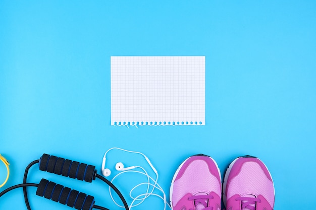 Empty white sheet of paper, pink sports sneakers and jump rope on a blue surface