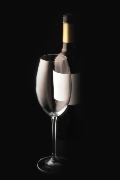 An empty wine glass and a bottle of red wine on a black background with an empty label minimalistic still life studio vertical photo