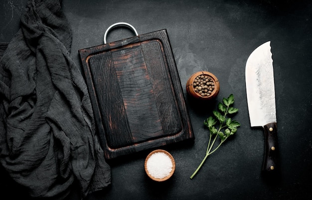 Empty wooden cutting board salt pepper and knife on black wooden table top view