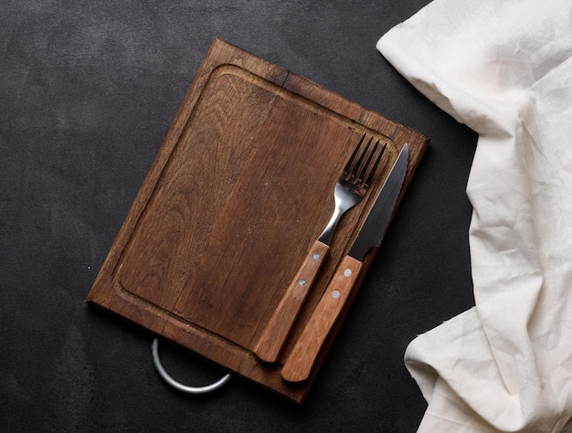 Empty wooden kitchen cutting board knife and fork with wooden handle on black background top view