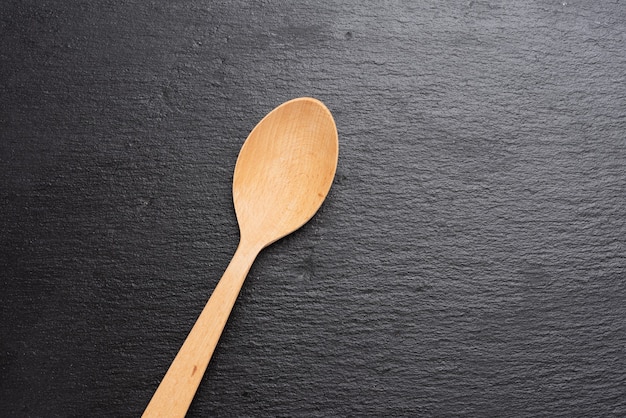 Empty wooden spoon on a a black surface, top view