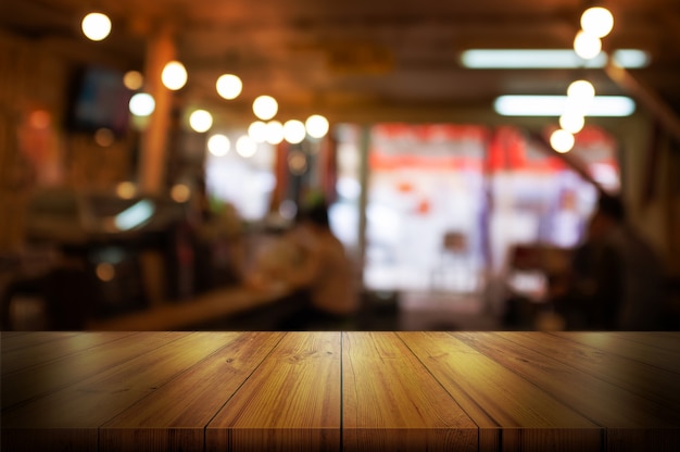 Empty wooden table top with blurred coffee shop or restaurant interior background. 