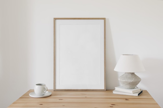 Empty wooden vertical picture frame mockup Cup of coffee on old books linen shade lamp on table White wall background Home office concept Elegant working space Scandinavian interior design