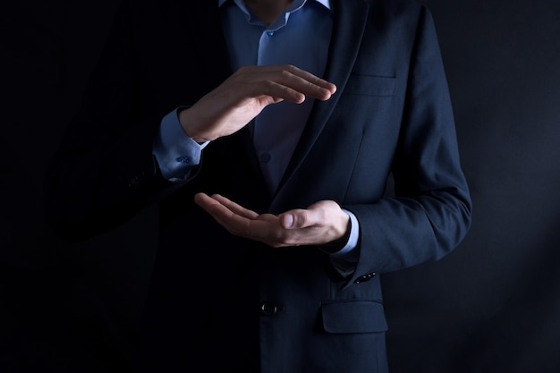 An empty workpiece. A businessman in a suit on a black background holds his hands protective gesture