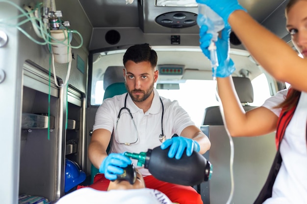 EMS Paramedics Team Provide Medical Help to Injured Patient on the Way to Healthcare Hospital Emergency Care Assistant Using Ventilation Mask in an Ambulance Young female nurse holding iv solution