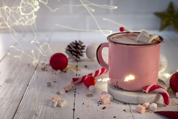 Enamel cup of hot cocoa with marshmallows and candy canes with beautiful Christmas lights