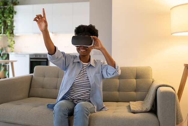 Encouraged African American woman using virtual reality glasses to watch 3D movies sits on sofa