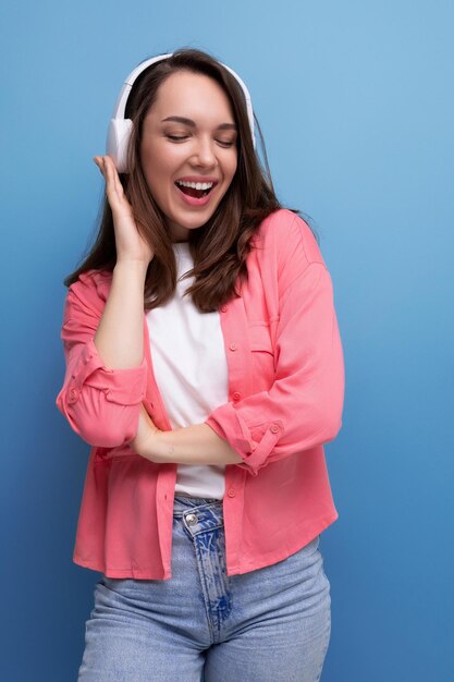 Energetic brunette young woman in a shirt and jeans listens to her favorite music on headphones