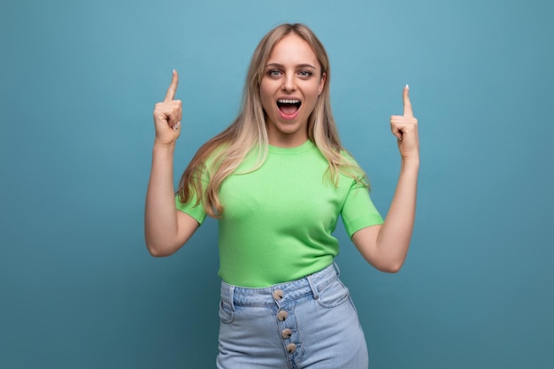 Energetic girl in casual outfit screaming joyfully pointing up on blue background